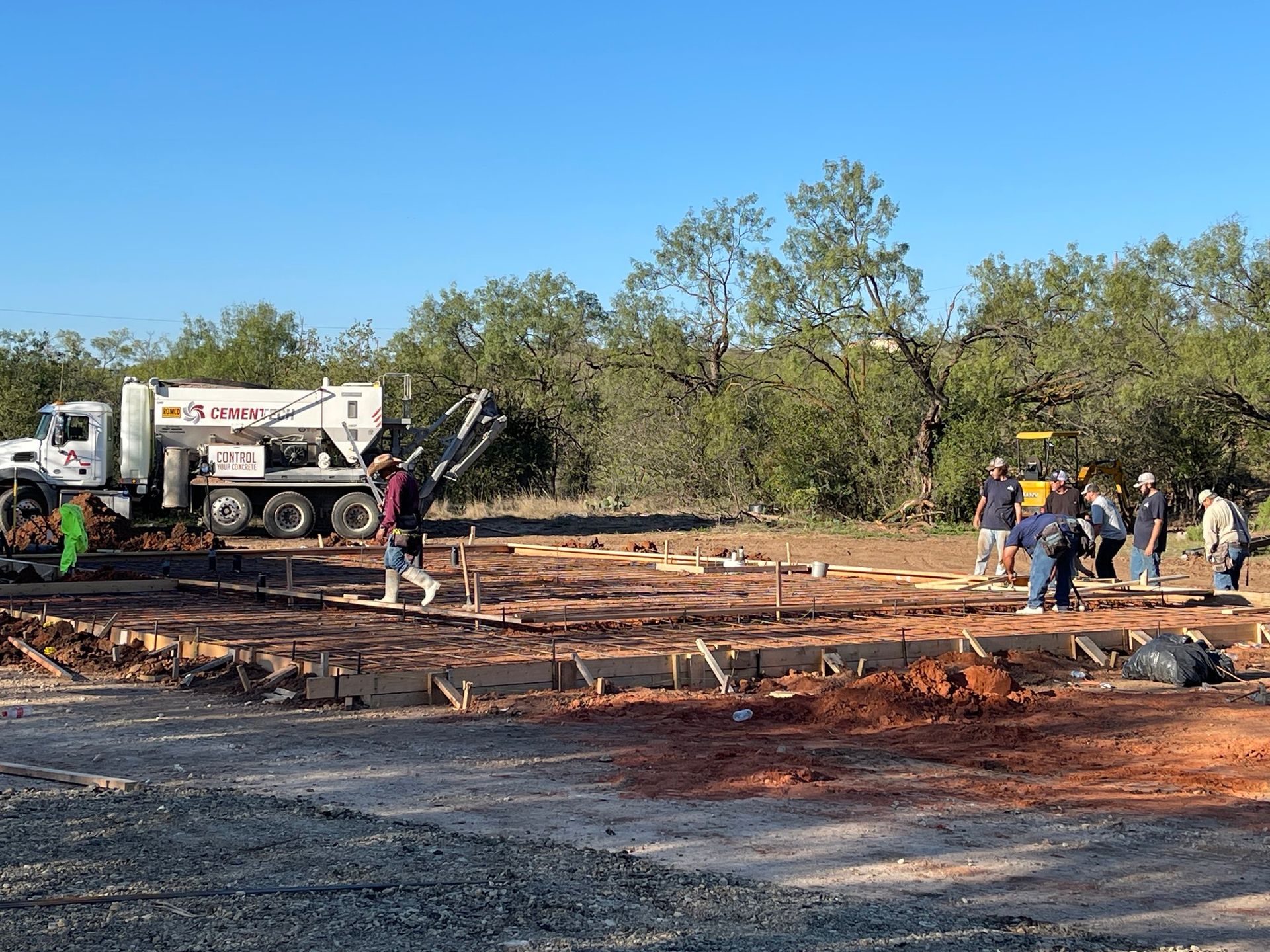 Construction crew pouring concrete on a foundation site beside a white work truck under a clear blue sky