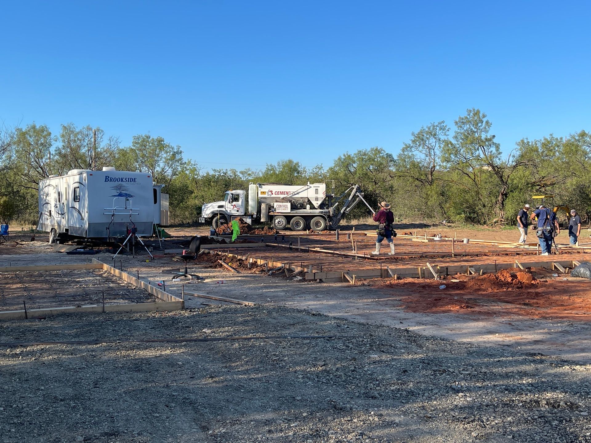 Burned outdoor lot with debris, trucks, and workers under a clear blue sky