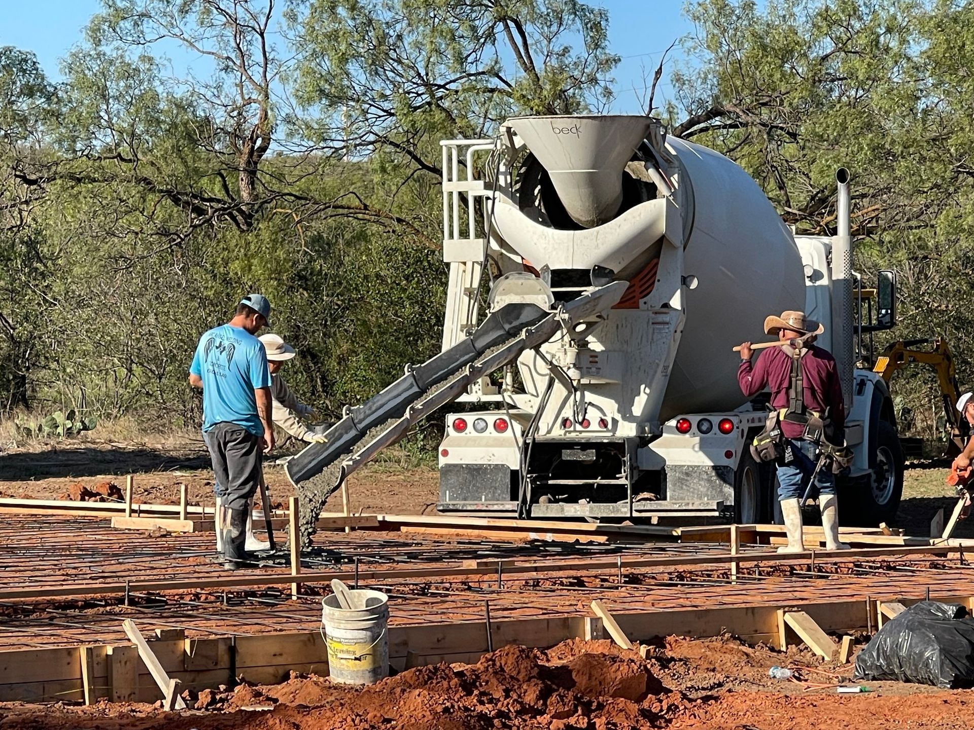 Concrete mixer truck on a construction site with workers pouring a slab.