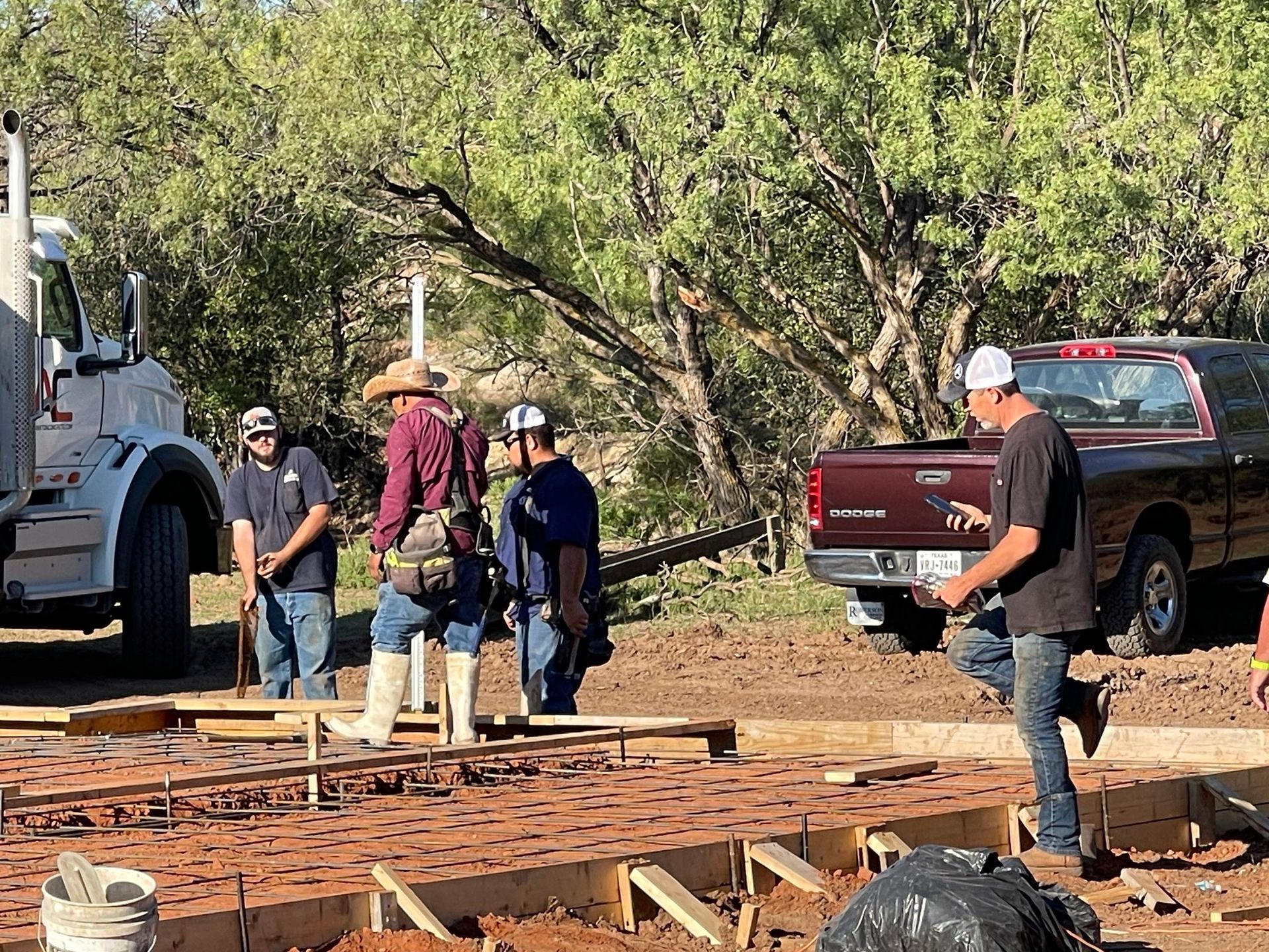 Workers on a construction site lifting lumber beside a pickup truck and heavy equipment.