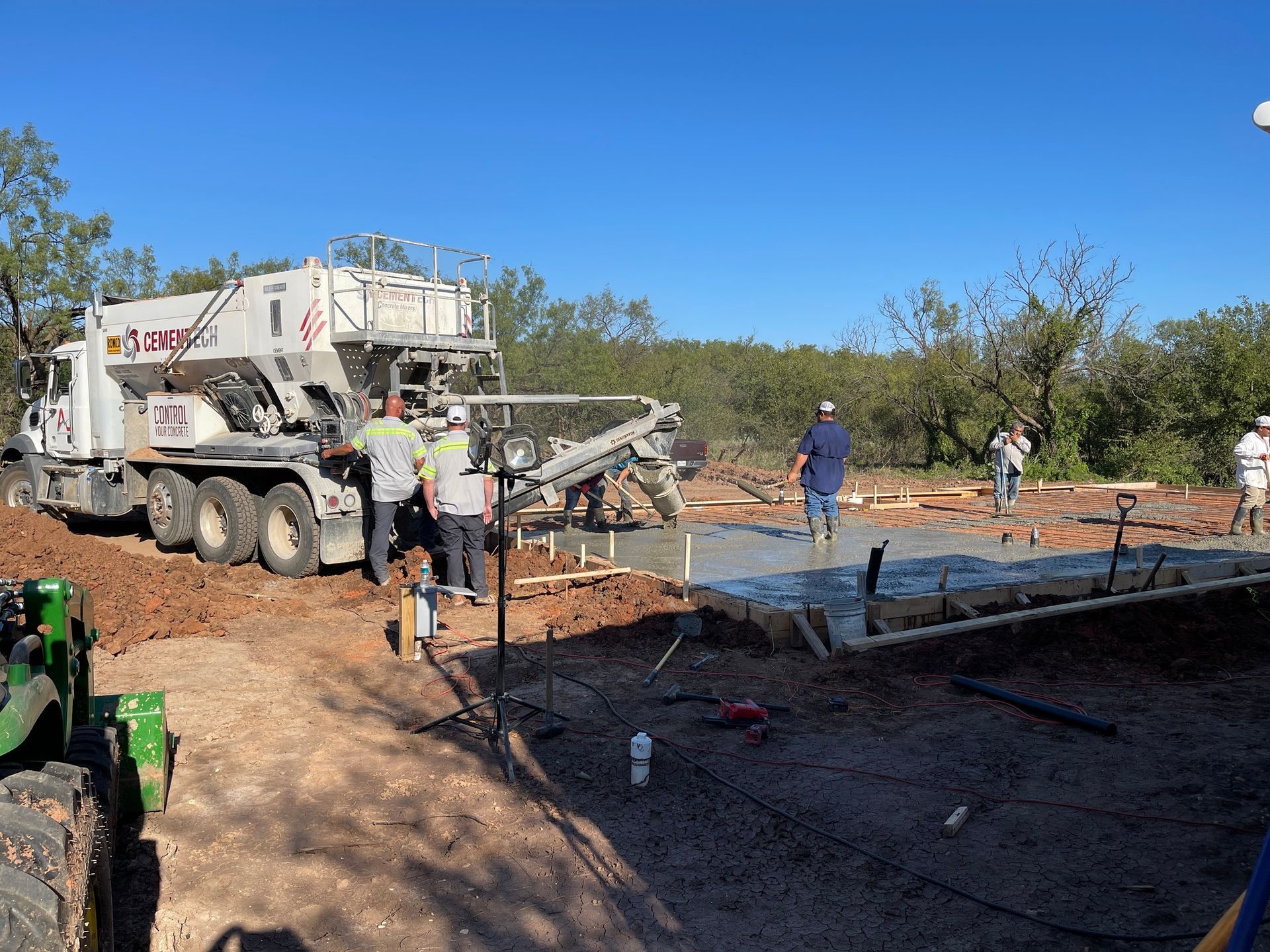 Concrete truck pouring foundation on a construction site with workers and rebar under a clear blue sky