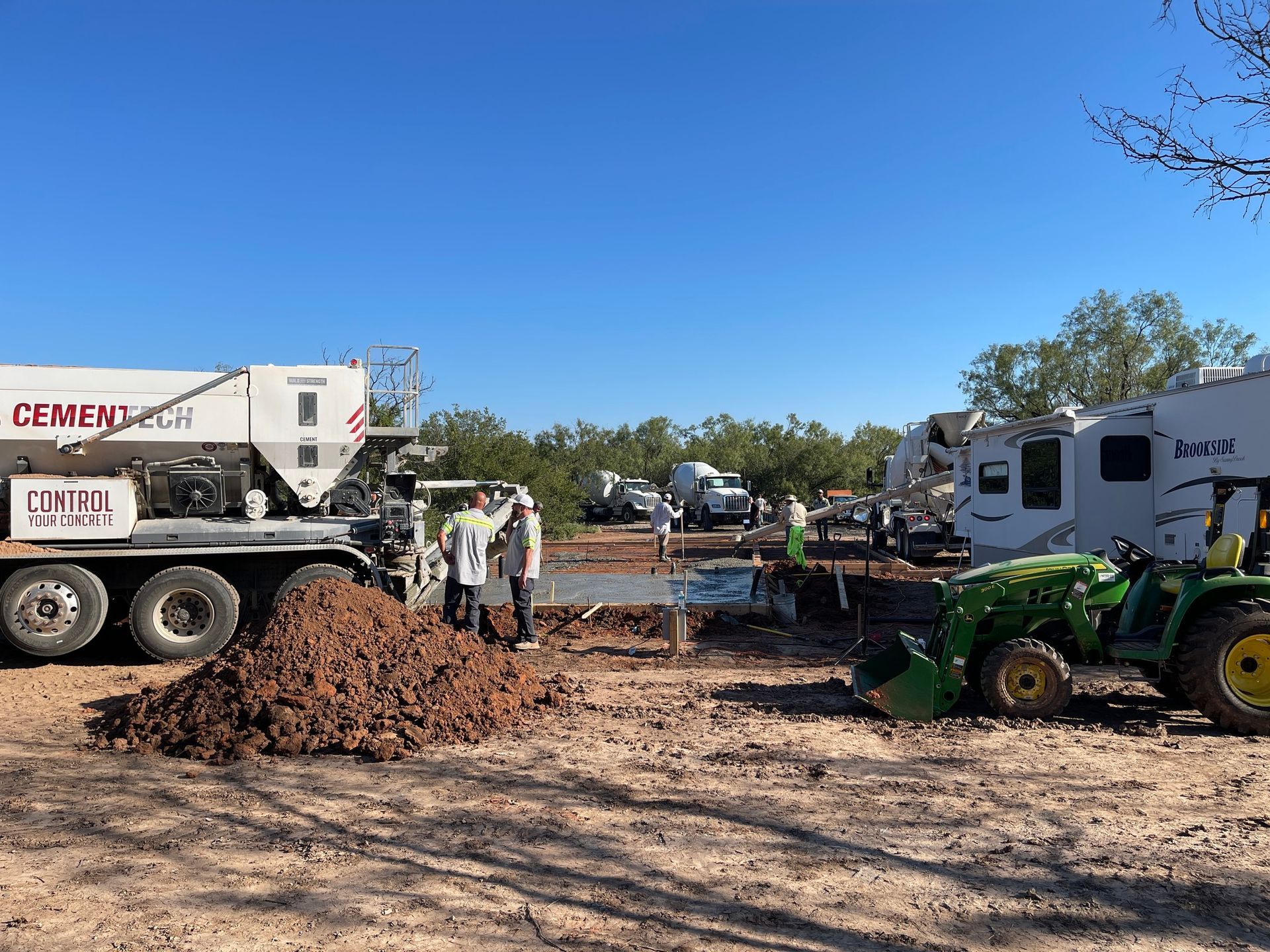 Construction site with dump truck, green tractor, workers, and a pile of dirt under a blue sky
