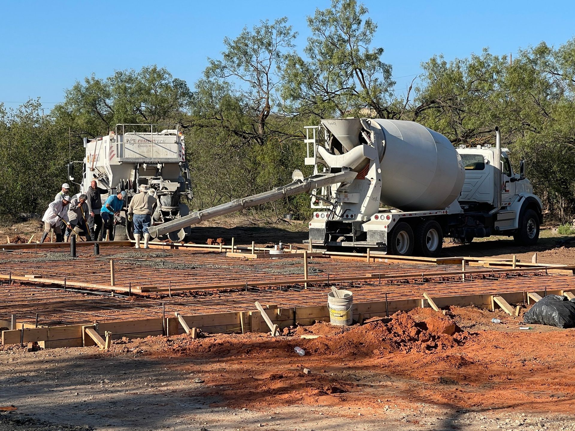 Workers pour concrete at a construction site using a cement mixer truck and pump hose.