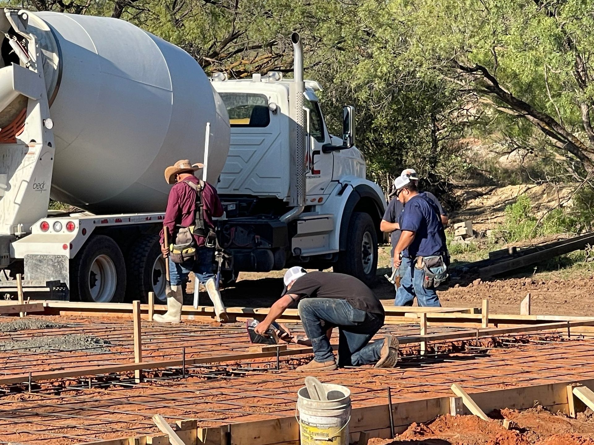 Construction crew pouring concrete at a rural site beside a cement mixer truck.