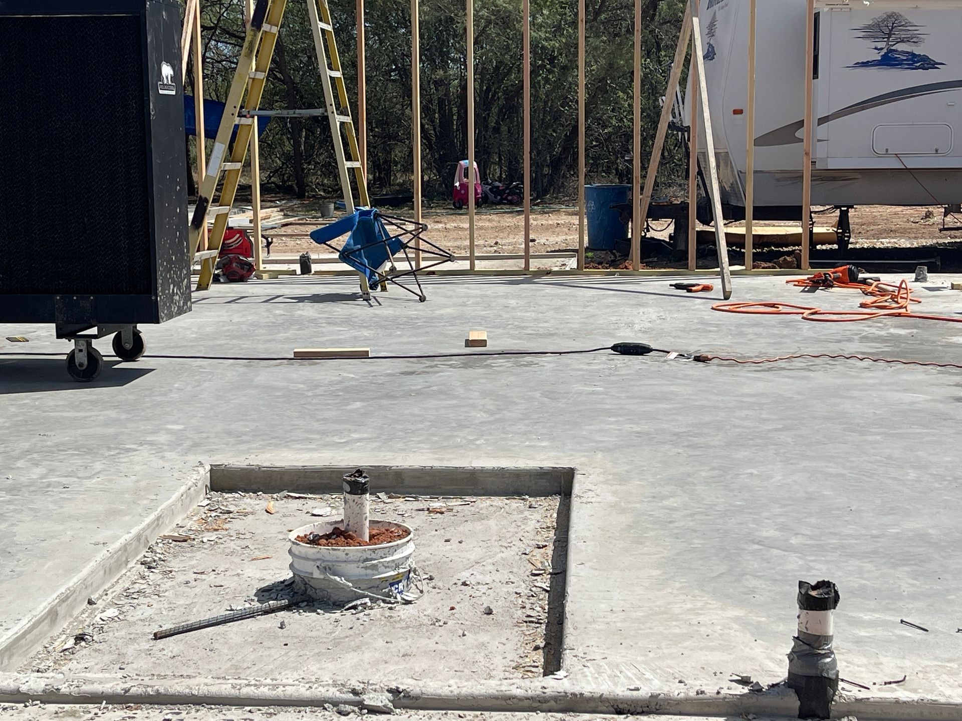 Construction site with concrete slab, exposed piping, and framed wall studs in the background