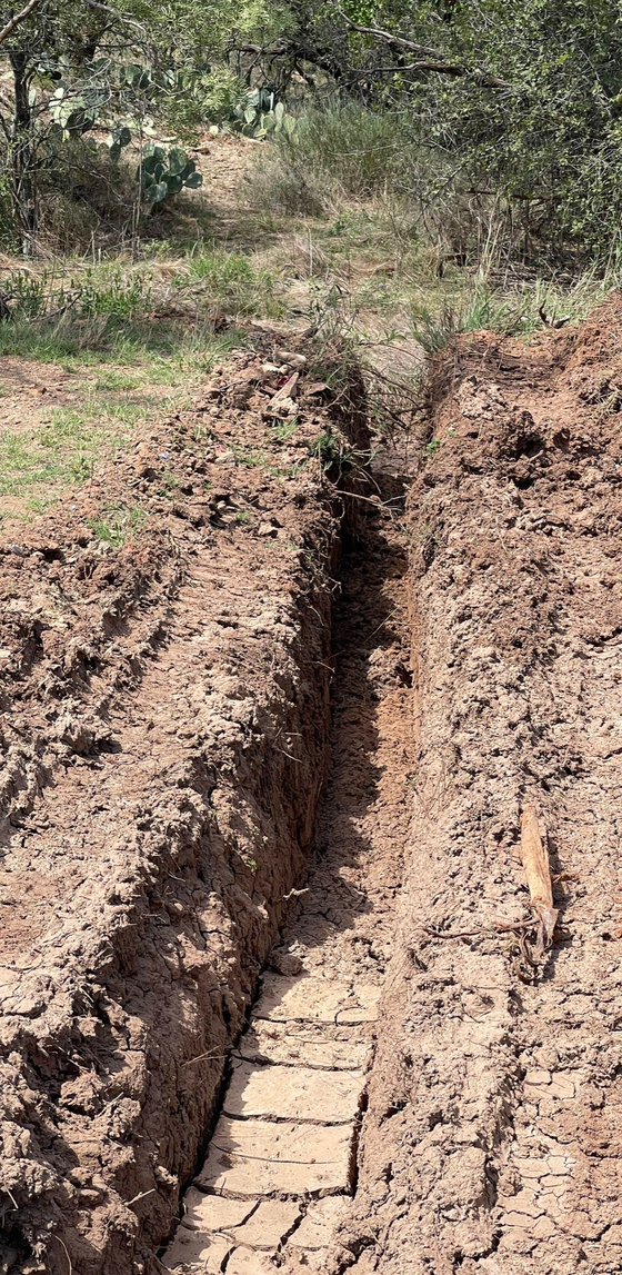 Deep trench cut through dry soil in a wooded outdoor area