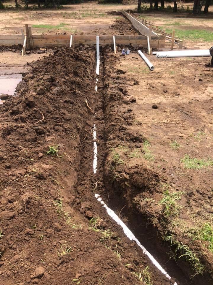 Trench dug through bare soil with white PVC pipe laid inside on a construction site