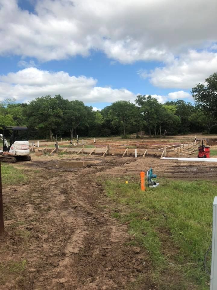 Dirt lot with a muddy track, construction forms, and trees under a cloudy sky