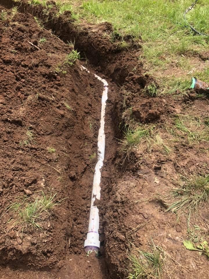 A white pipe runs through a narrow trench in brown soil and grass.