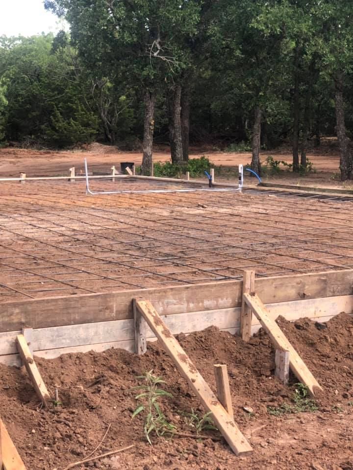 Partially built concrete foundation with wooden formwork and dirt foreground near trees