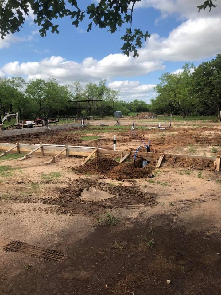 Construction site with wooden foundation forms and dirt work under a partly cloudy sky.