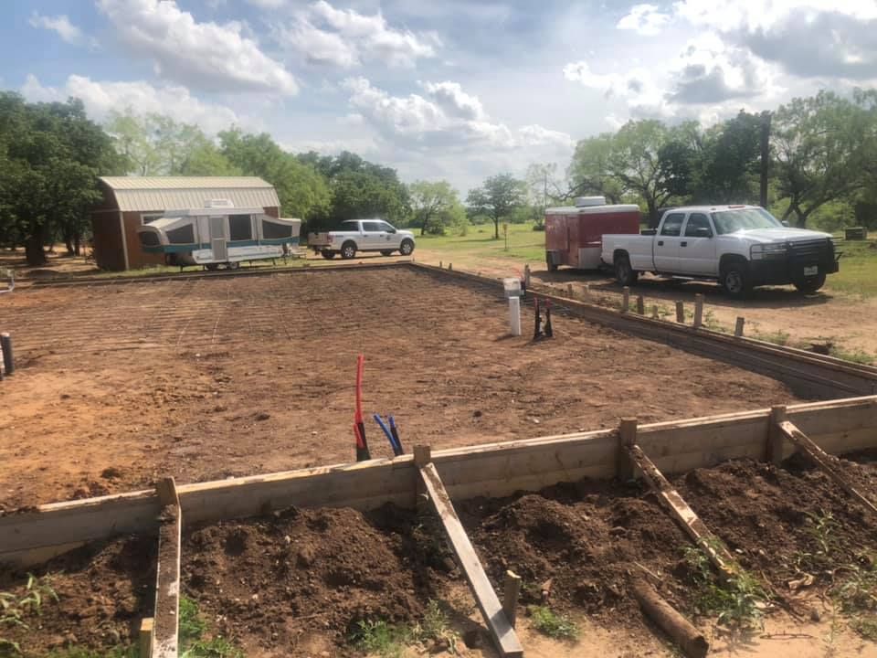Construction site with concrete foundation forms, dirt lot, and pickup trucks under a cloudy sky