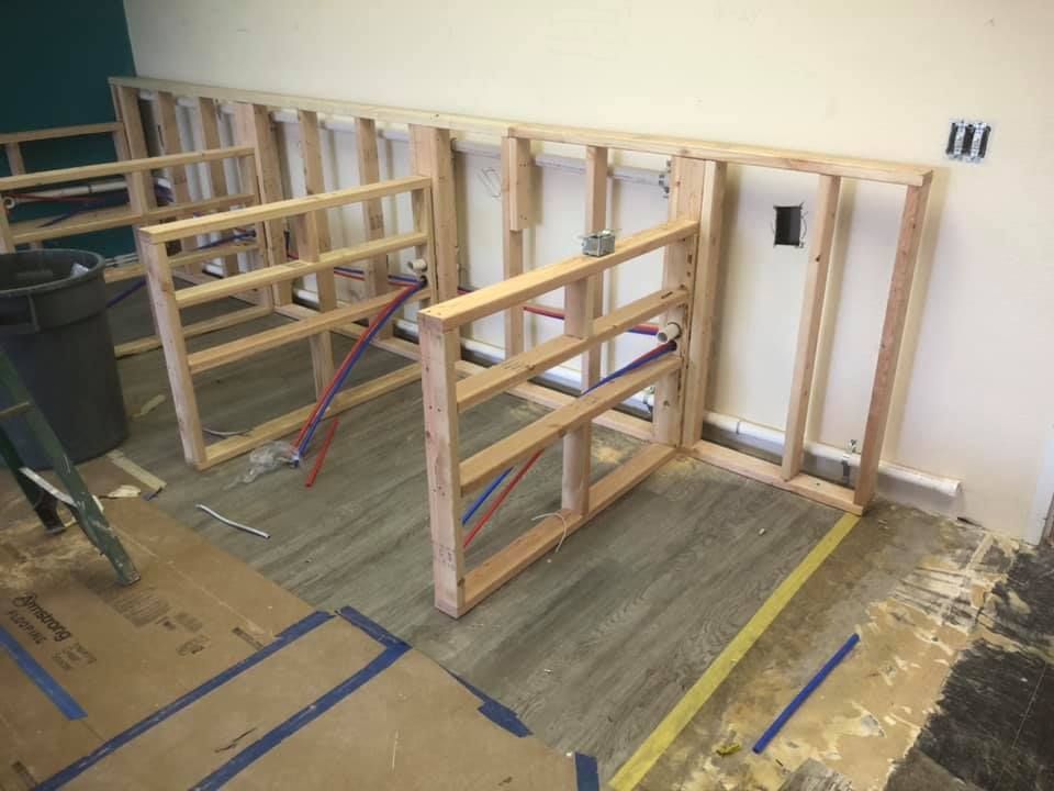 Wooden wall framing under construction in an unfinished room with blue tape on the floor