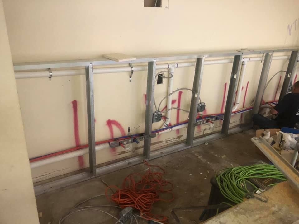 Bathroom wall with exposed plumbing, red and green pipes, and construction tools on the floor