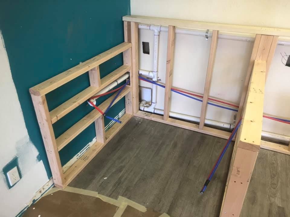 Unfinished room with wooden framing, teal wall, and a small built-in shelf by the corner.