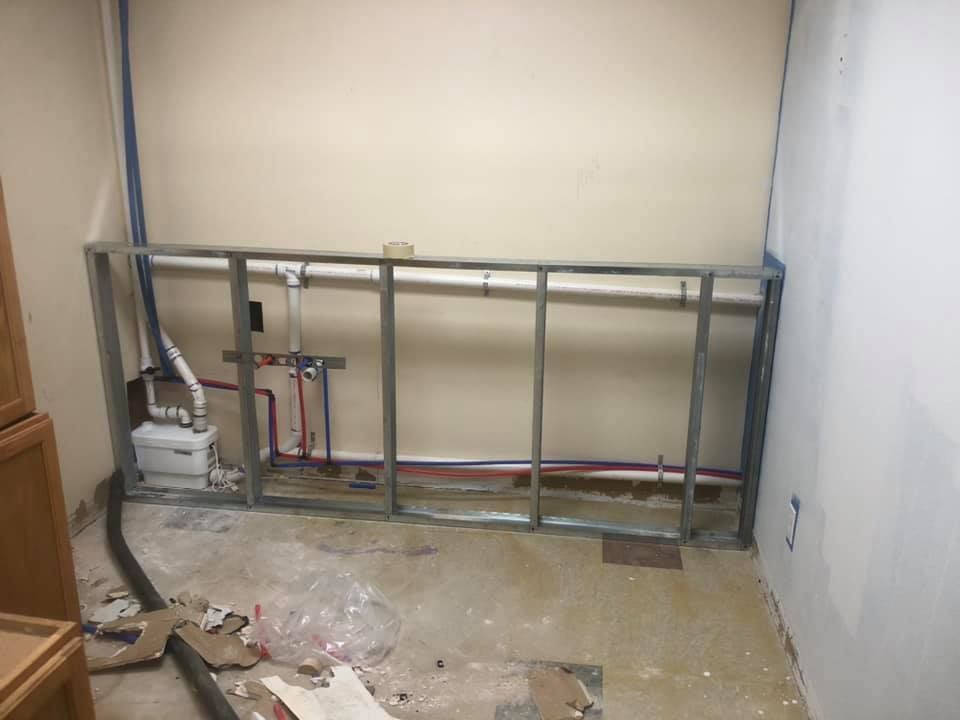 Partially assembled metal wall frame in a bare room with exposed plumbing and construction debris on the floor