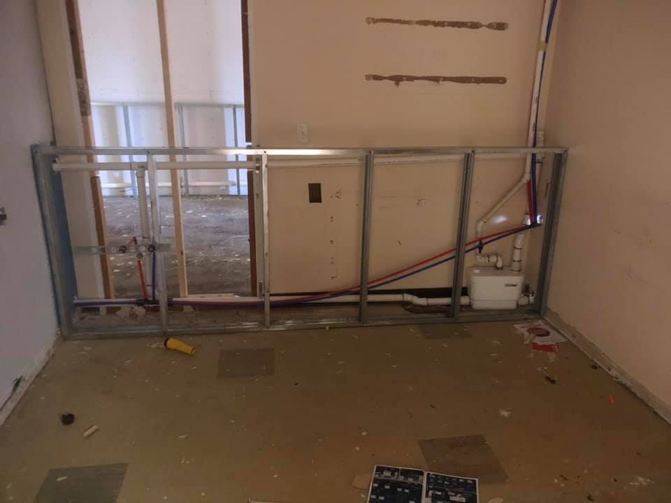 Empty room with a partially built metal railing leaning against the wall and exposed wiring on the floor.