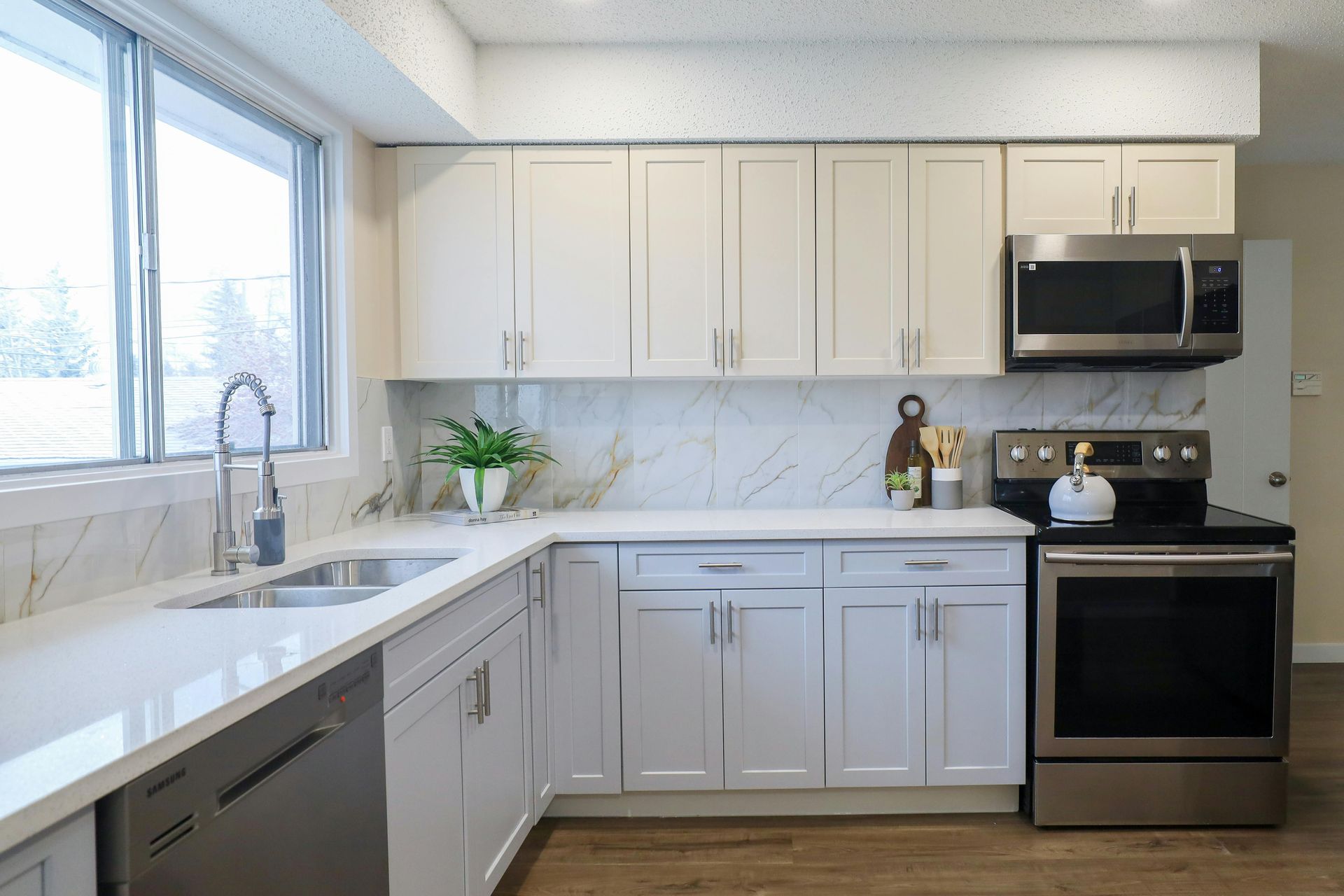 Bright white kitchen with stainless appliances, large window, and wood floor