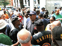 Large crowd of people gathered outdoors; several men in hats, including one with a