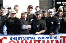 Sheet metal workers in black shirts shaking hands in front of a banner that reads