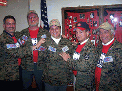 Five people in camouflage and red shirts pose together in front of US flag and display.