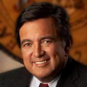 Smiling man in a suit, headshot. Brown hair, dark eyes.