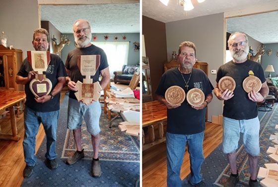 Two men holding woodworking awards, standing in a room with wood furniture, various woodworking tools, and wood pieces.