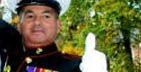 Man in dark uniform with medals, white gloves, and a hat. Set against foliage.