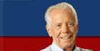 Smiling older man against a blue and red background.
