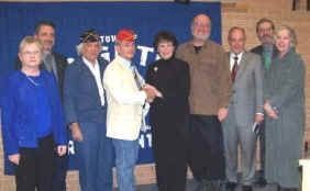 Group of people posing, some shaking hands, in front of a blue backdrop with text.