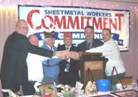 Group of men with hands together in front of a banner that reads