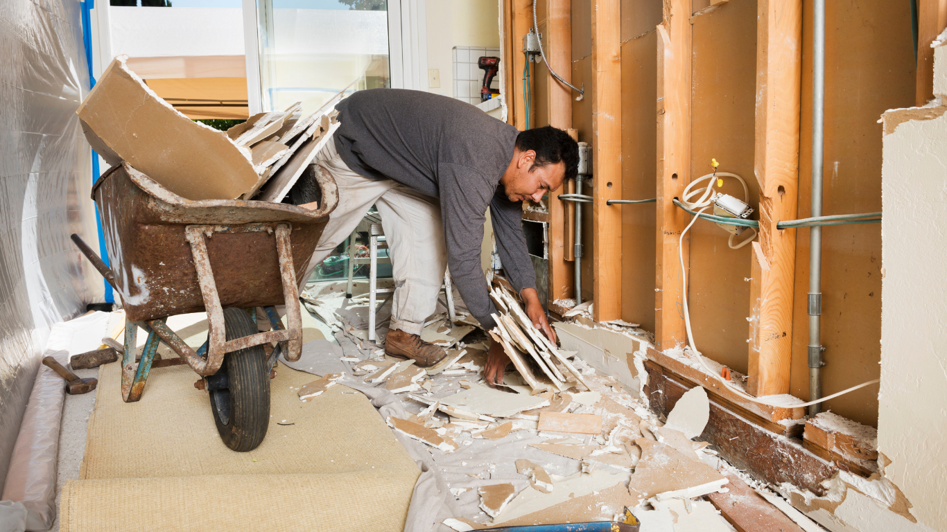 A man is doing interior demolition in a house with a wheelbarrow.