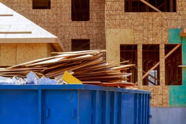 A blue dumpster filled with wood is in front of a house under construction. - debris cleanup