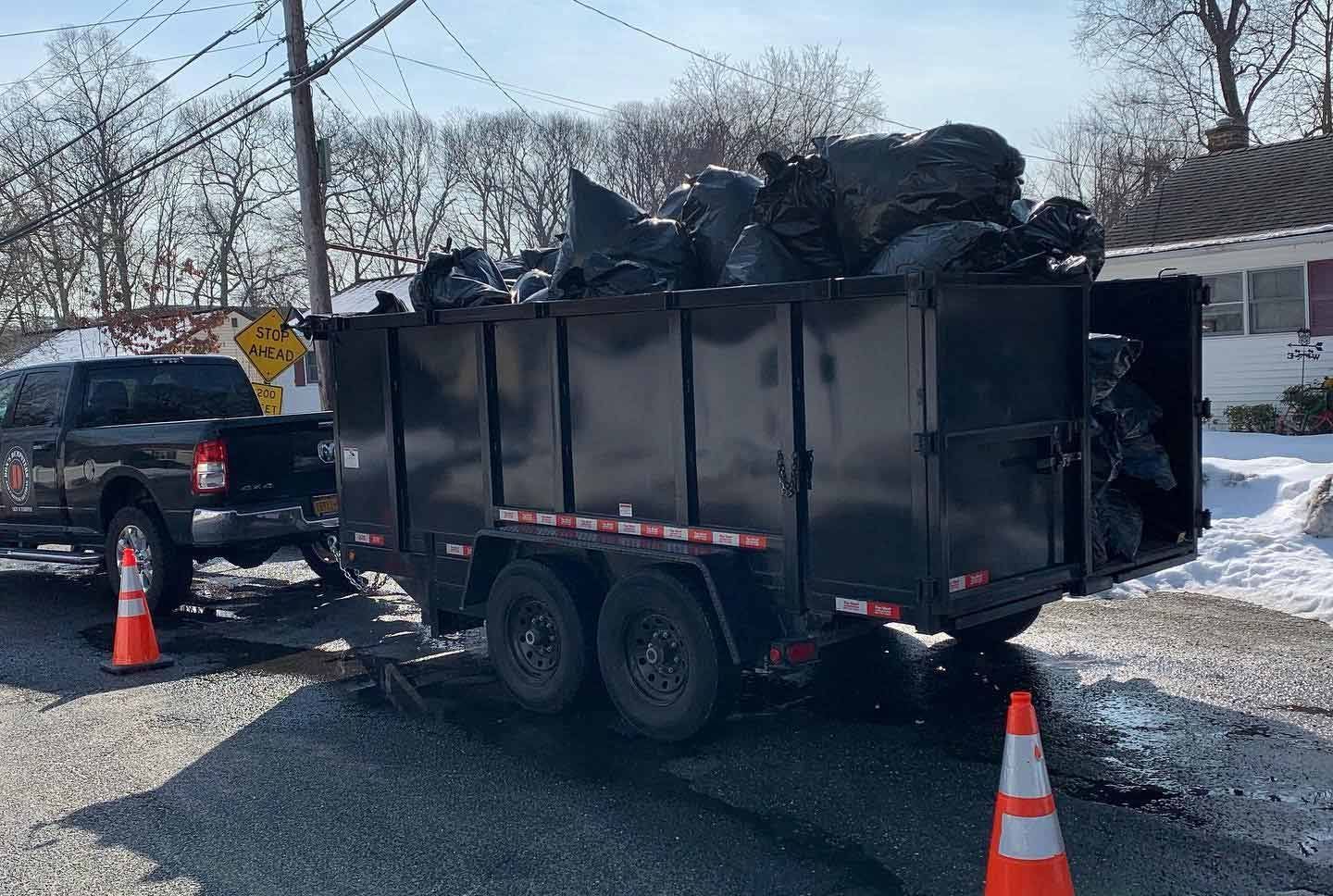 A dumpster trailer filled with trash bags is parked on the side of the road. - junk removal