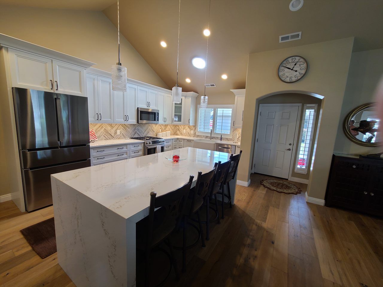 A kitchen with white cabinets , stainless steel appliances , a large island and a clock on the wall.