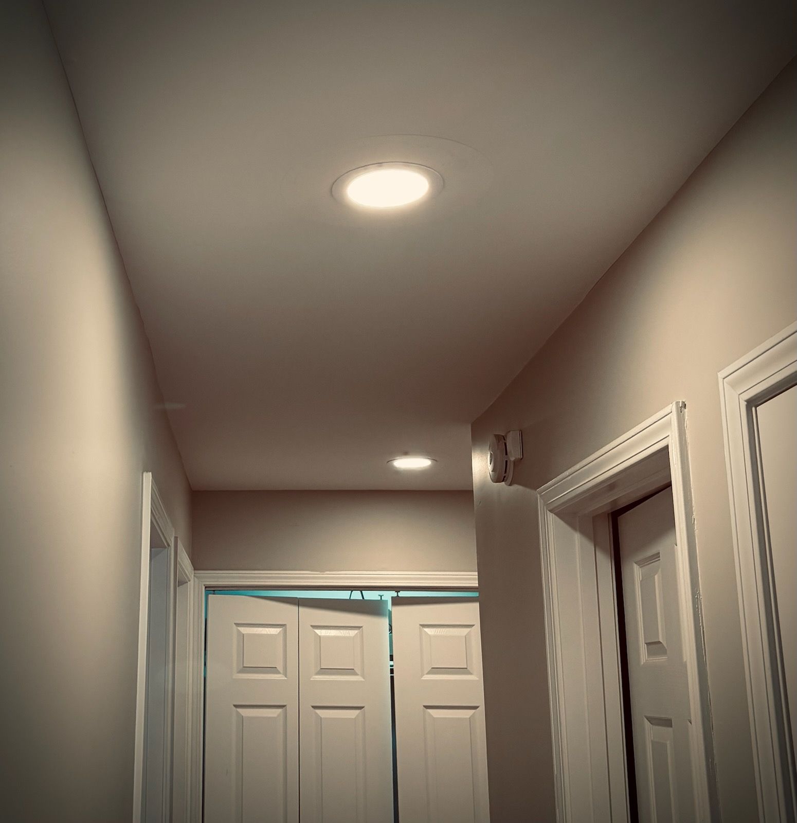 Narrow beige hallway with white doors and recessed ceiling lights.