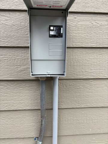 Outdoor electrical meter box mounted on a house wall with conduit pipes below