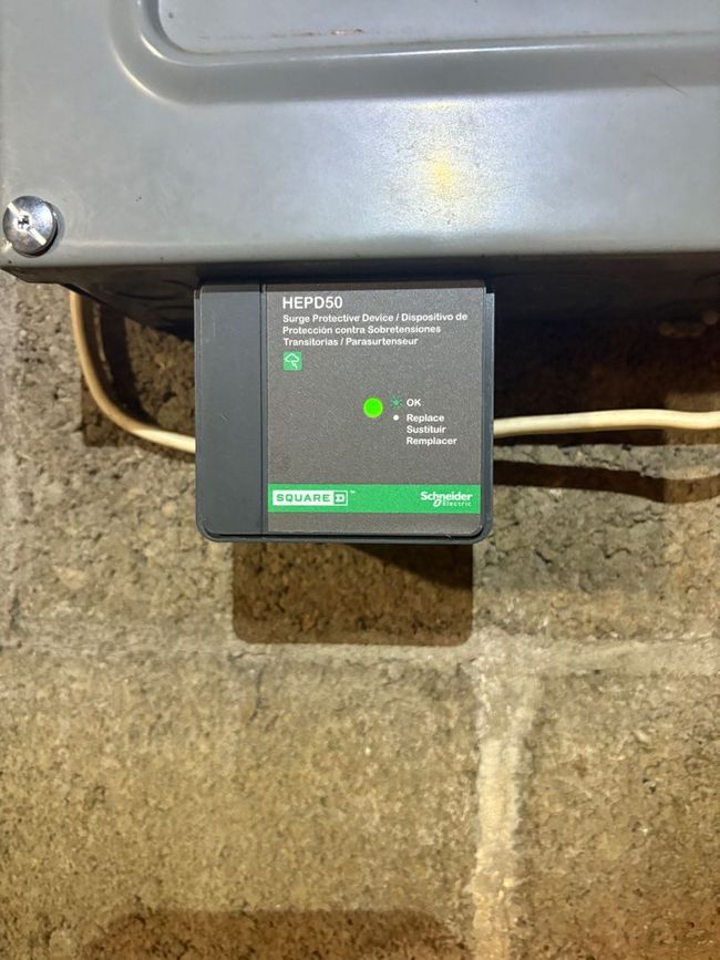 Black square control module with green indicator lights mounted under a metal appliance.