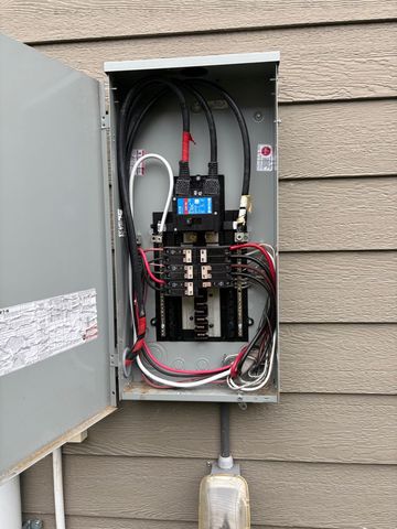 Open electrical breaker panel with red and black wiring on an exterior wall