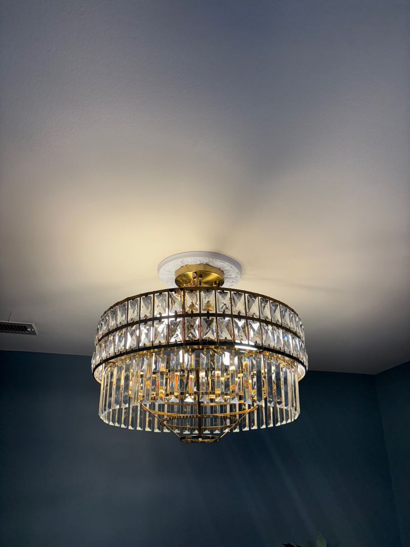 Crystal chandelier ceiling light glowing against a dark blue ceiling with a halo of warm light.