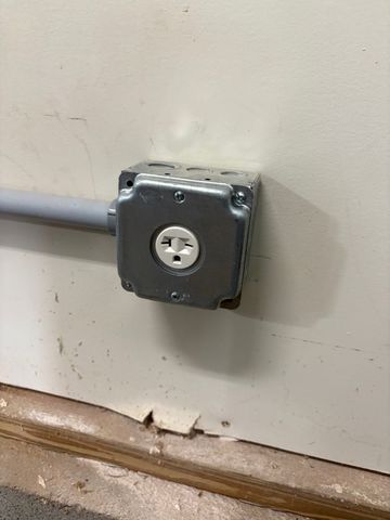 Gray metal electrical outlet box mounted on a wall with conduit attached.
