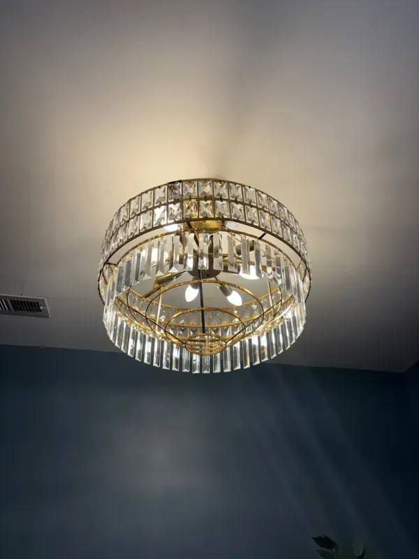 Crystal chandelier ceiling light with warm glow against a blue wall and white ceiling