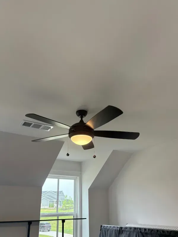Ceiling fan with light in a sloped white room above a window and railing