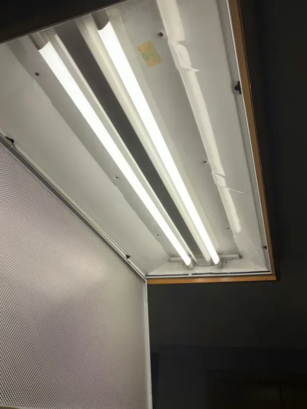 Open fluorescent light fixture in a ceiling panel above a textured wall.