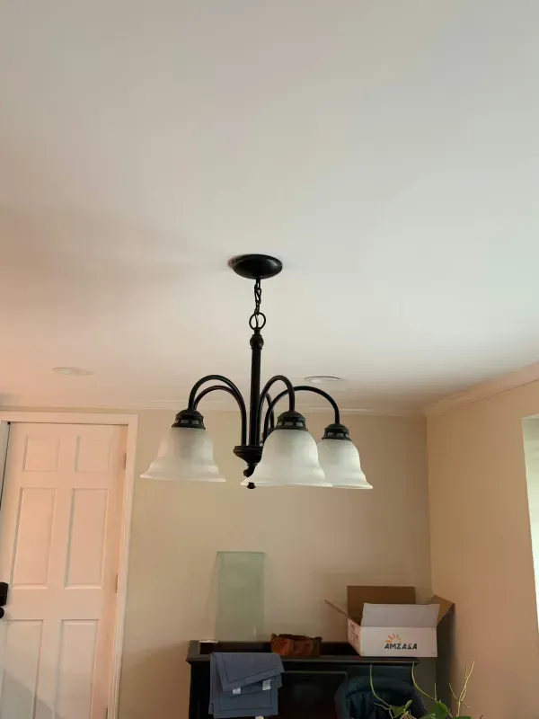 White dining room with a black chandelier and frosted glass shades above a table with boxes.
