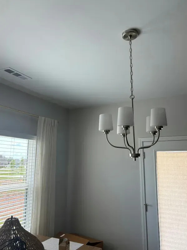 Dining room with a white chandelier, gray walls, window blinds, and a table beneath the light.
