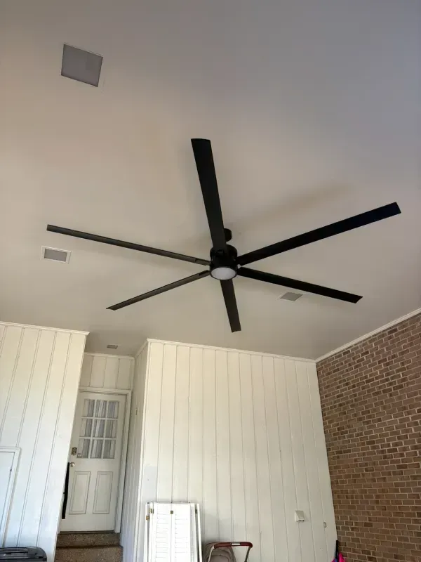 Covered patio ceiling with large black ceiling fan, white walls, and a door at the back