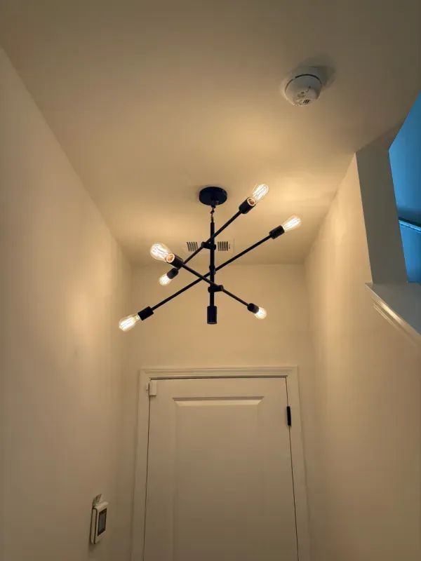 Modern black starburst chandelier on a white hallway ceiling above a closed door