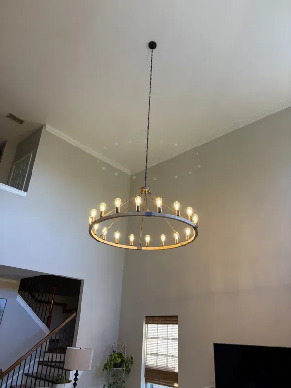 Modern living room with high ceiling, large round chandelier, staircase, and wall-mounted TV.