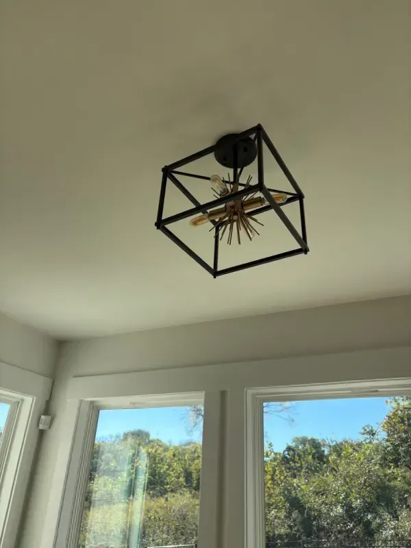 Black geometric ceiling light fixture with exposed bulb on a white ceiling above windows.